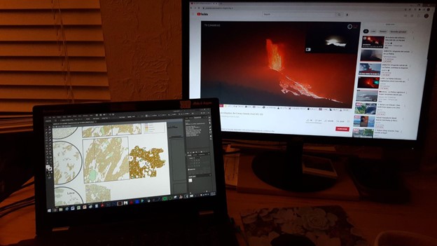 An image of Olivia's desk, showing a laptop screen on the left where she is constructing a new figure and a computer screen on the right where she is watching the live stream of the eruption on YouTube.