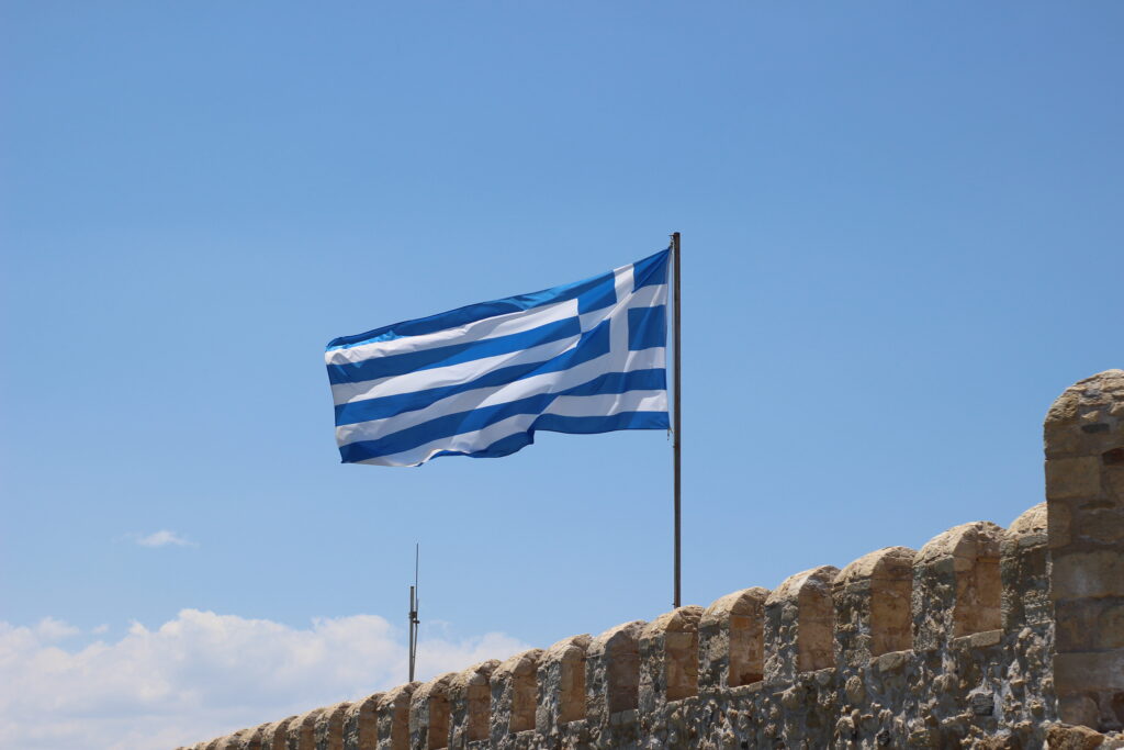 The Greek flag blowing in the wind against a blue sky.