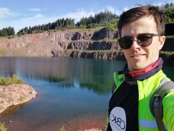 Sam Poppe wearing sunglasses, taking a selfie in front of a quarry and body of water.